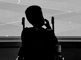 black and white image of Charlie Ellacot in a wheelchair looking out on to a football pitch